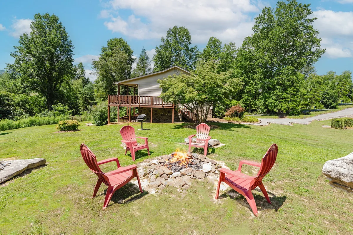 A cozy fire pit surrounded by vibrant red chairs, set against a backdrop of the main house and lush landscape. The area is designed for group gatherings, storytelling, and classic campfire moments under the open sky.