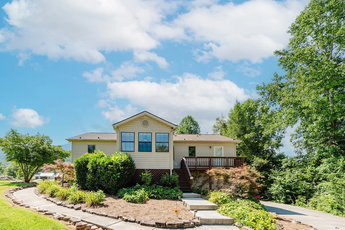 This exterior image displays the inviting facade of the property, featuring a welcoming porch, landscaped garden, and the driveway that leads directly to the house. The setting is tranquil with well-maintained greenery, suggesting ease of arrival and a peaceful start to any stay.