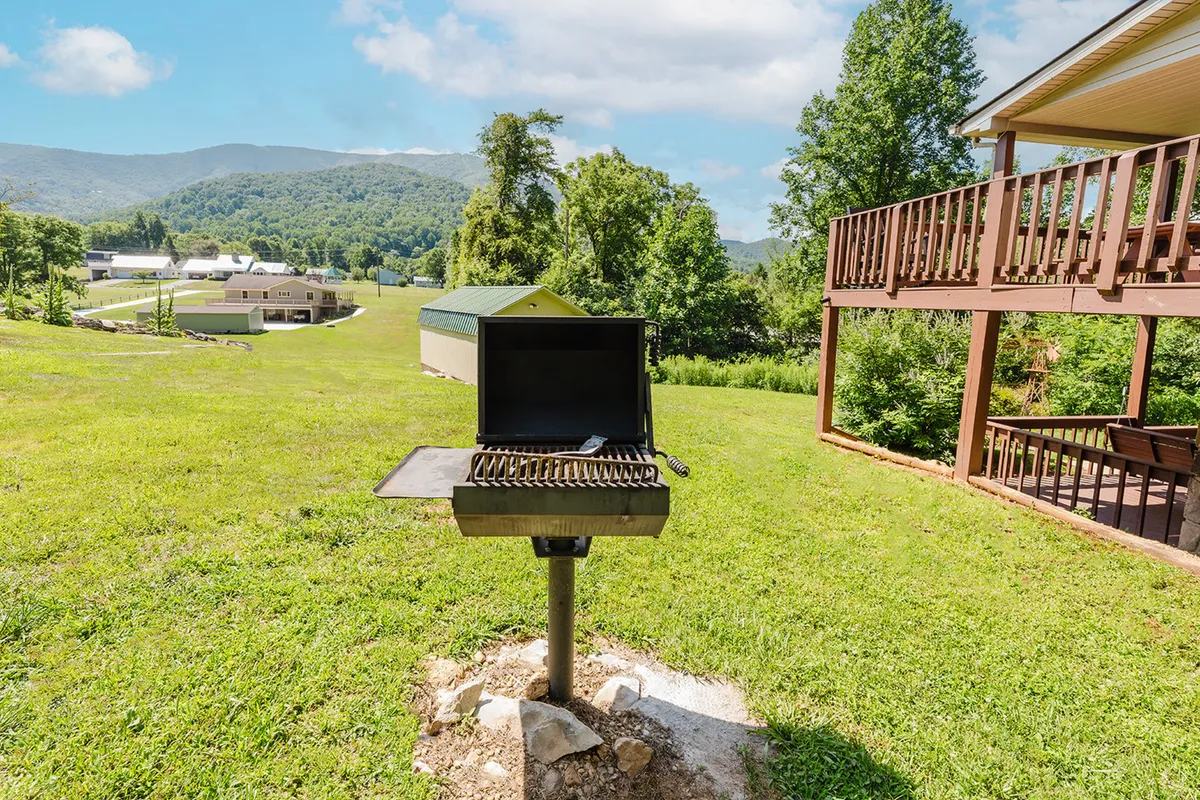 A charcoal grill is set up on the deck overlooking a stunning mountain backdrop, with ample space for outdoor dining and relaxation. The scene captures the essence of outdoor cooking and eating amidst beautiful scenery.