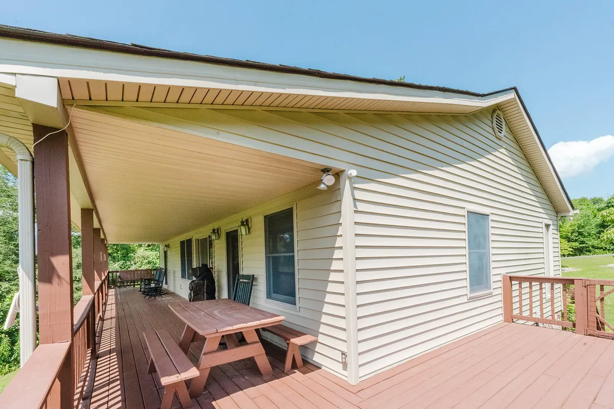 A casual deck area is shown with a picnic table, the exterior walls of the house, and abundant outdoor space for group dining or relaxing in the shade. The setup is ideal for al fresco meals and socializing.
