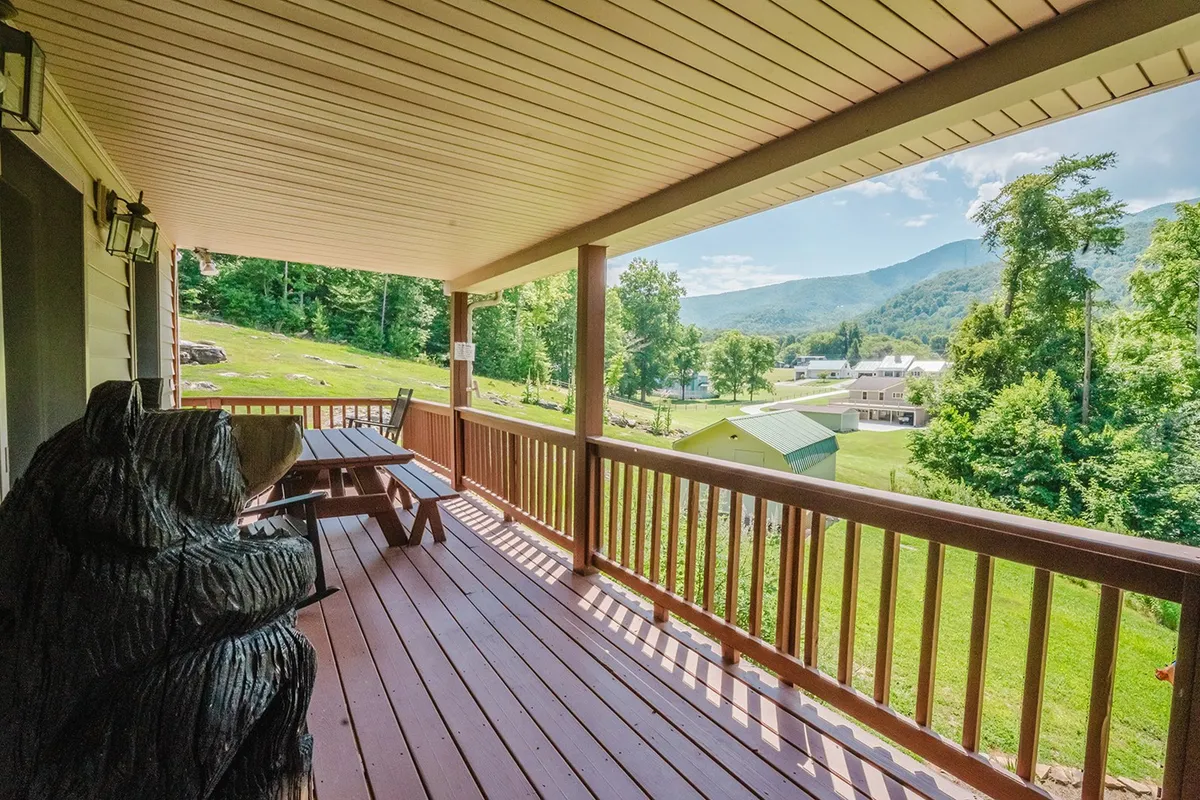 A spacious porch with wooden railings and outdoor seating, overlooking stunning mountain views. A whimsical bear sculpture adds a touch of local charm, while the setting invites relaxation and social gatherings in the fresh mountain air.