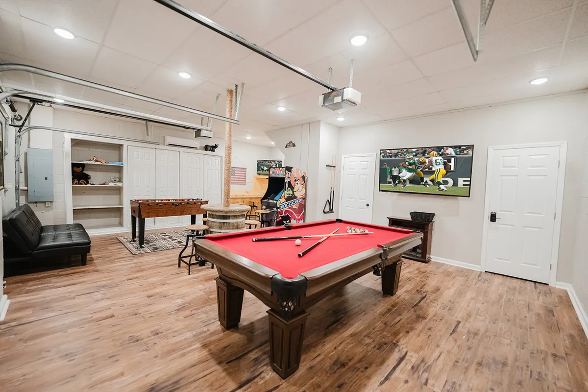 Inside, a vibrant game room is equipped with a pool table, arcade game, cozy seating, and a wall-mounted TV. The arrangement invites groups to compete in friendly games, watch TV, and relax together.