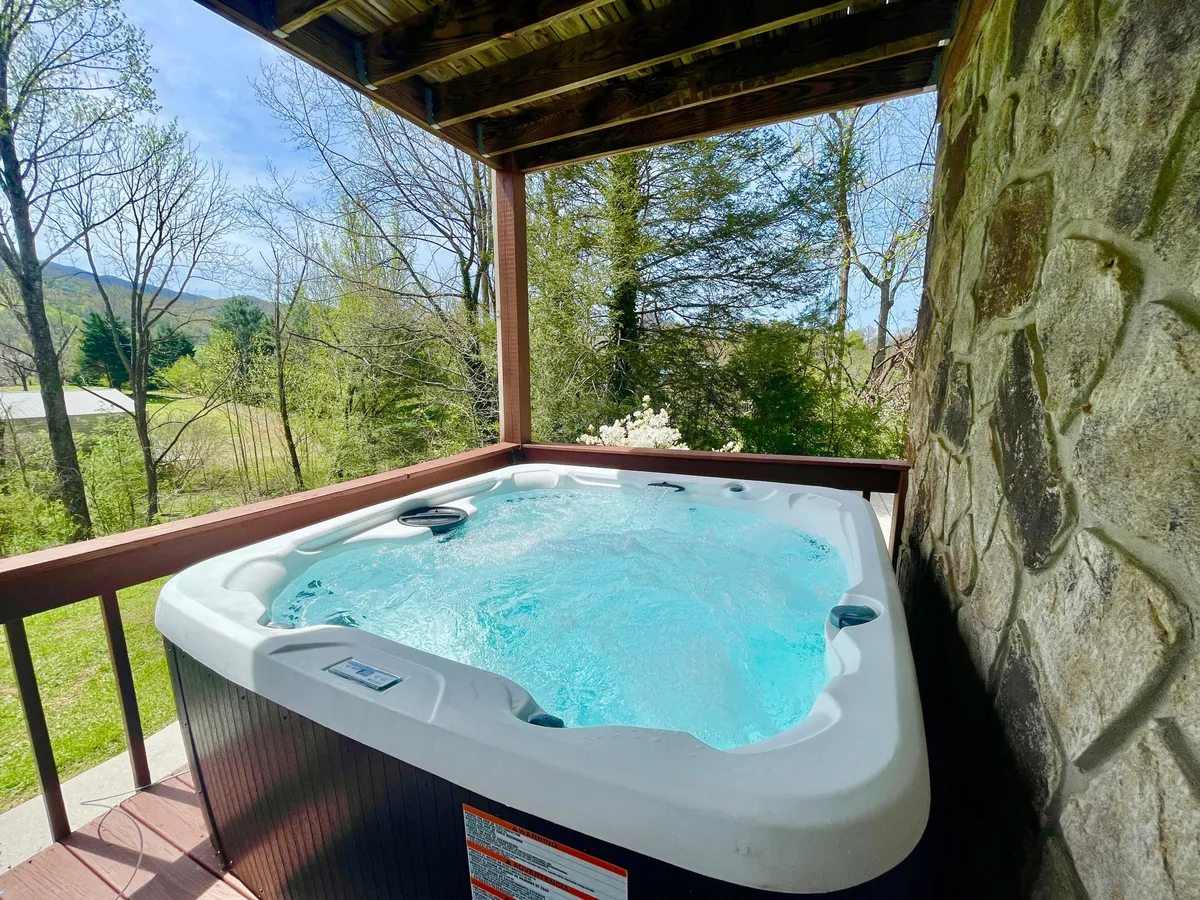 A cozy hot tub nestled on a stone patio, surrounded by lush greenery. The setting is peaceful, inviting guests to relax and unwind while taking in the sounds and views of nature.